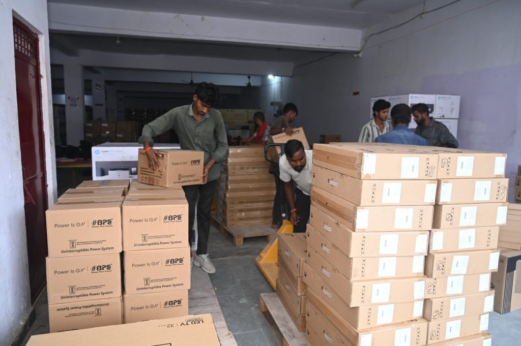 Group of workers in a dim warehouse moving and stacking large brown cardboard boxes on pallets and aisles.