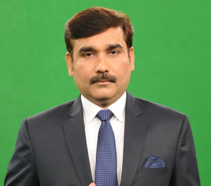 dilip tiwari | No. 1 Indian Media News Portal Man in a dark suit with white shirt and blue polka-dot tie, standing against a green backdrop.
