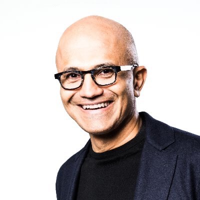Smiling man with black-framed glasses wearing a dark blazer against a white background, portrait-style headshot.