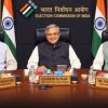 Three men sit at a conference table in the Election Commission of India office, with Gyanesh Kumar, Chief Election Commissioner, centered; Indian flags and the EC backdrop behind them.