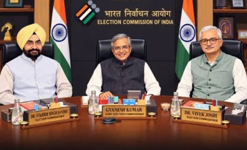 eci_1 | No. 1 Indian Media News Portal Three men sit at a conference table in the Election Commission of India office, with Gyanesh Kumar, Chief Election Commissioner, centered; Indian flags and the EC backdrop behind them.