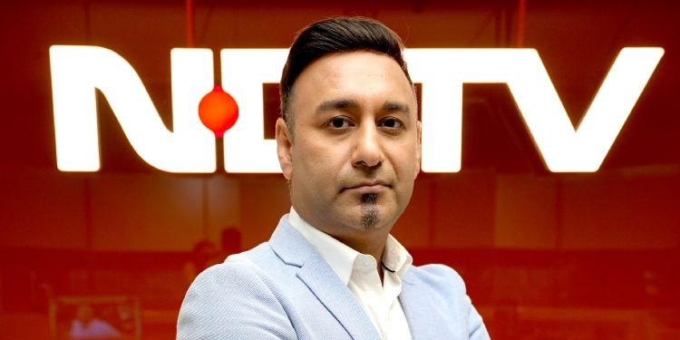 Head-and-shoulders portrait of a man in a light blue blazer in front of a NETV logo backdrop.