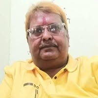 Man with glasses and mustache wearing a yellow polo shirt indoors, with a tilak on his forehead.
