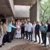 Group of people in casual and traditional attire standing at a construction site, forming a line and shaking hands in the center.