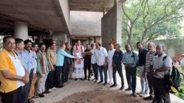 Group of people in casual and traditional attire standing at a construction site, forming a line and shaking hands in the center.