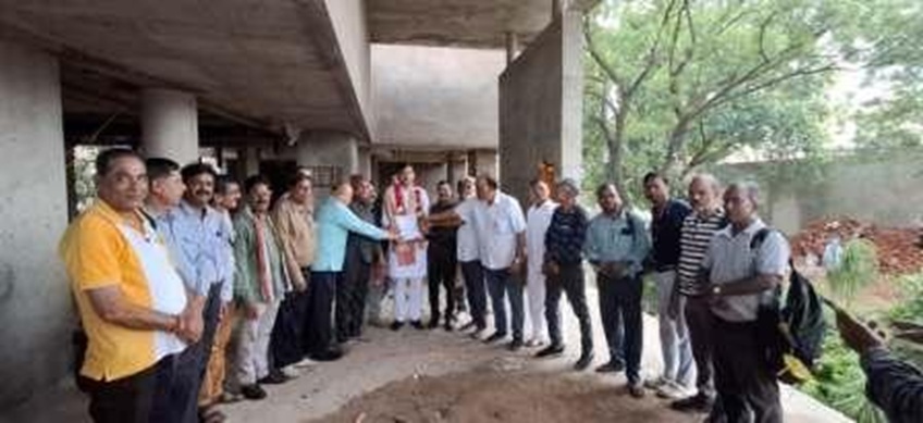 Group of people in casual and traditional attire standing at a construction site, forming a line and shaking hands in the center.