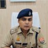 Police officer in khaki uniform with beret, seated at a desk in an office.