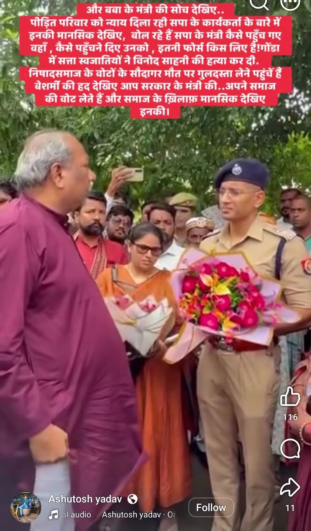 Man in a maroon kurta hands a bouquet to a uniformed police officer as a crowd looks on during an outdoor event.