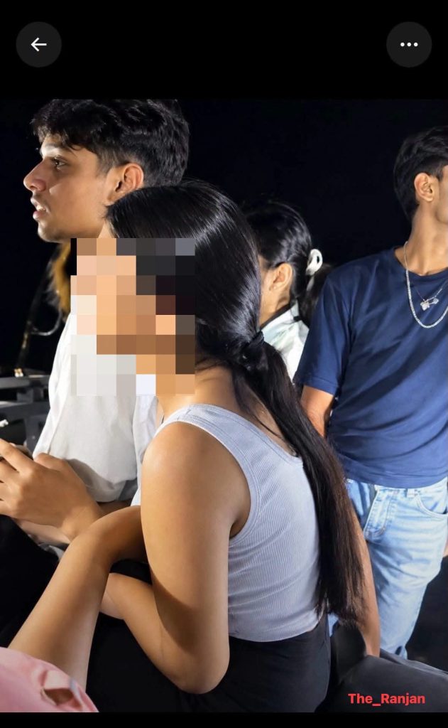 img_1354 | No. 1 Indian Media News Portal Group of young people sitting side by side at night; foreground woman with long black hair in a gray tank top, a man next to her with a blurred face, watermark The_Ranjan bottom right.
