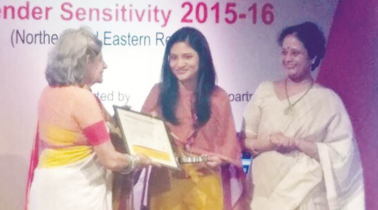 img_1389 | No. 1 Indian Media News Portal Three women on stage during an award ceremony; an older woman hands a certificate to a smiling young woman while another woman watches.