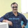 Portrait of a man in a blue denim shirt wearing sunglasses, smiling in an office with a Hindi name overlay: मनिष श्रीवास्तव