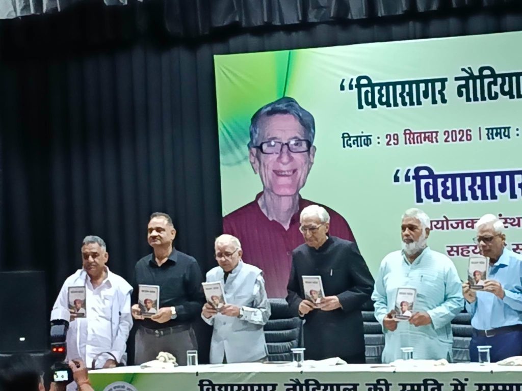 kajal kotha_3 | No. 1 Indian Media News Portal Group of men on a stage holding books during a book launch event, with a large banner featuring a portrait in the background.