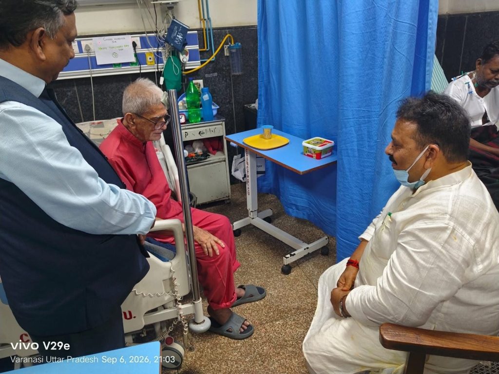 lahiri_ravindra | No. 1 Indian Media News Portal Elderly man in red seated in a hospital room while a visitor stands nearby and a nurse sits in front, with a blue privacy curtain in the background.