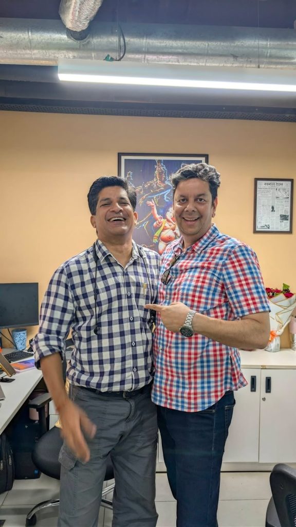 lalit | No. 1 Indian Media News Portal Two men in plaid shirts smiling in an office, one pointing at the other, with a computer and framed artwork behind them.