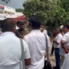 A group of men in white shirts stand in a circle outdoors, talking near a campus or government building with trees in the background (video still).