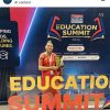 Woman in a red sari holding a trophy in front of a large 'EDUCATION SUMMIT' banner at an event.
