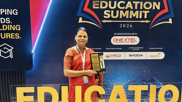 Woman in a red sari holding a trophy in front of a large 'EDUCATION SUMMIT' banner at an event.