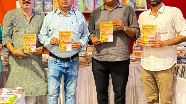 Four men stand in a bookstore display, each holding a yellow-covered book with a man on the cover, shelves of books behind them.
