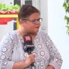 Woman wearing glasses and a patterned blouse is being interviewed, speaking into a News18 microphone outdoors with a potted plant in the background.