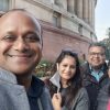 Four friends take a group selfie outside a large red-stone building, smiling at the camera.