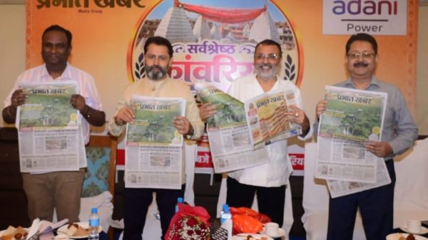 Four men stand side by side, each holding a copy of a newspaper at a press event, with a Prabhat Khabar backdrop and Adani Power logo behind them.