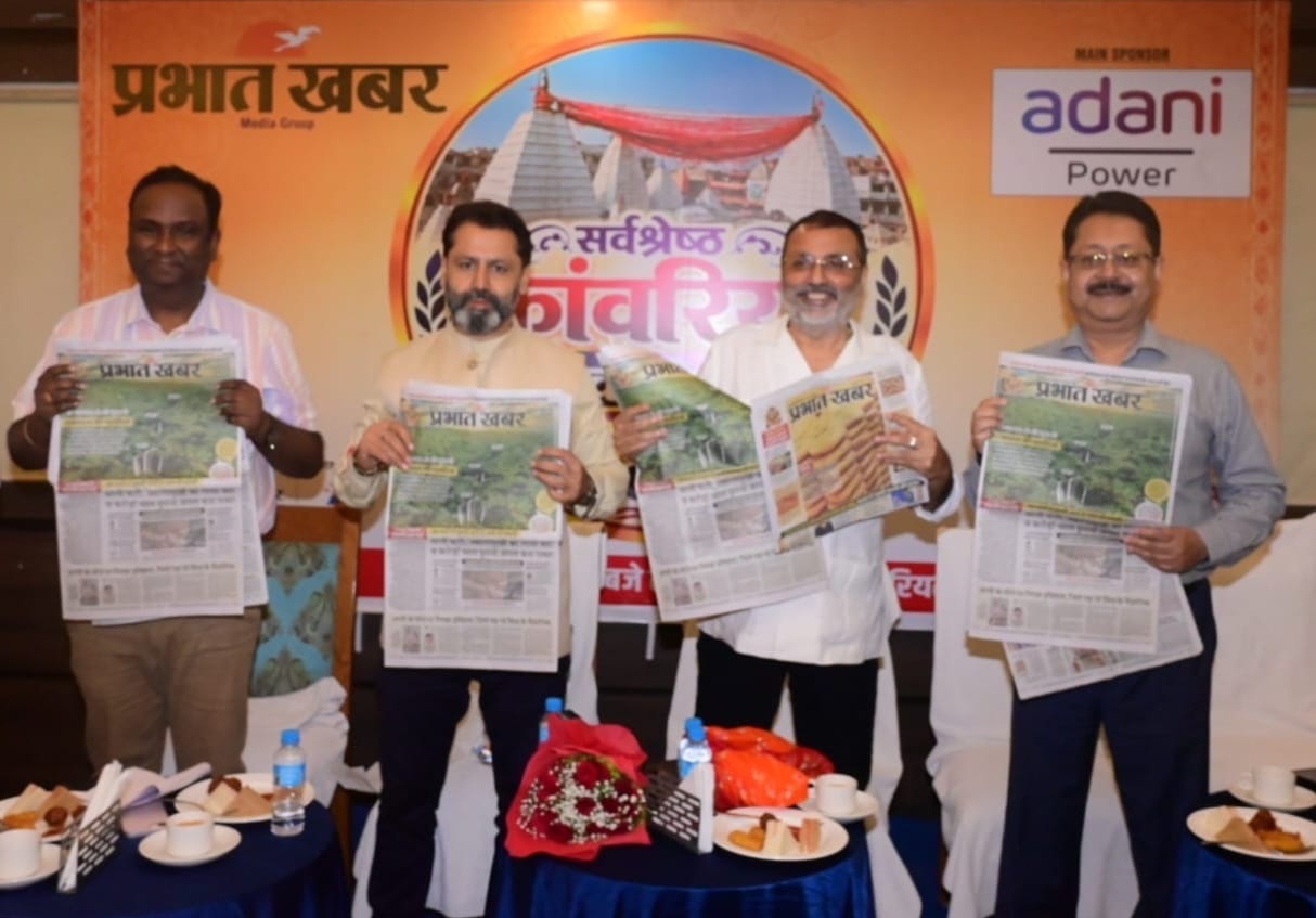 Four men stand side by side, each holding a copy of a newspaper at a press event, with a Prabhat Khabar backdrop and Adani Power logo behind them.