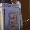 An elderly man speaks at a podium next to a large poster showing his portrait on a book cover.