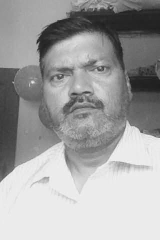 Black-and-white portrait of a middle-aged man with short dark hair and a beard, wearing a light shirt, looking at the camera with a serious expression.
