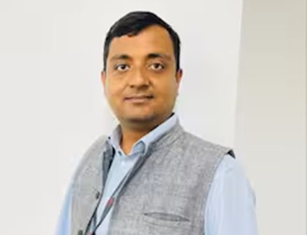 Man in a light blue shirt and gray vest posing for a professional photo indoors.