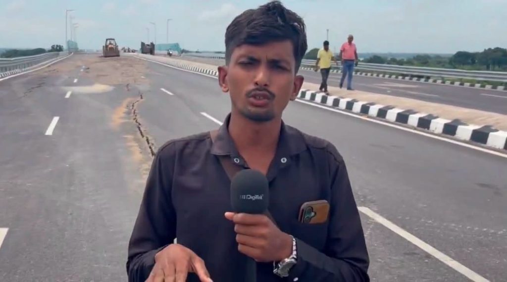 Screenshot | No. 1 Indian Media News Portal A young male reporter holding a microphone on a dusty, partially paved highway with construction vehicles in the distance.