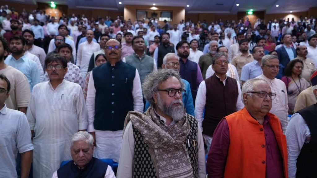rb rai_1 | No. 1 Indian Media News Portal Large indoor gathering of Indian men and women standing together at a formal event, with one seated elderly man in the foreground and another in a bright orange vest to the right.