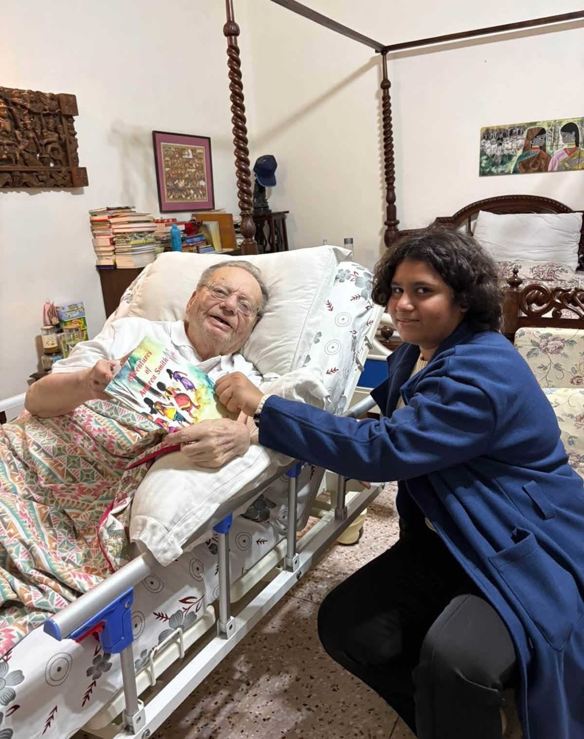 Elderly man in a hospital bed smiling as a younger person in a blue jacket reads him a colorful children's book from close up.