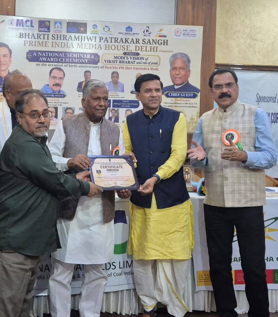 sanjai_ | No. 1 Indian Media News Portal Group of men on stage exchanging a certificate at an award ceremony, with a banner in the background and attendees watching nearby