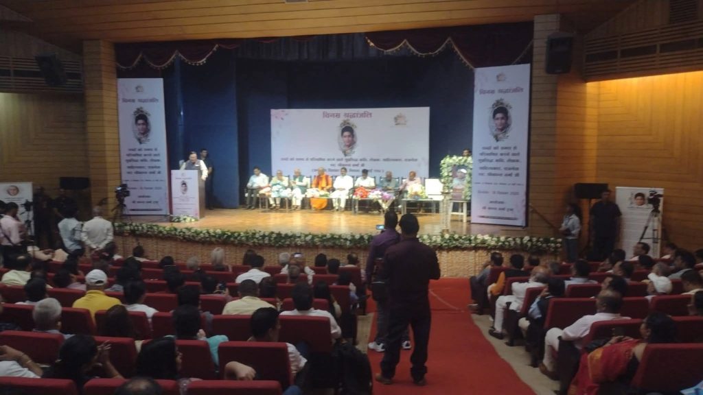 srikant shikhar | No. 1 Indian Media News Portal Stage with a panel of speakers seated on chairs, a podium on the left, banners flanking the stage, and an audience in red seats below.