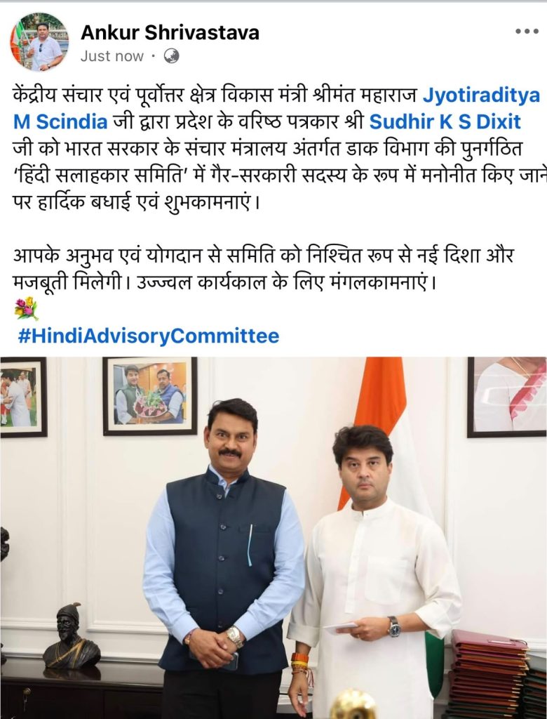 Two men in formal attire posing in an office with an Indian flag in the background.
