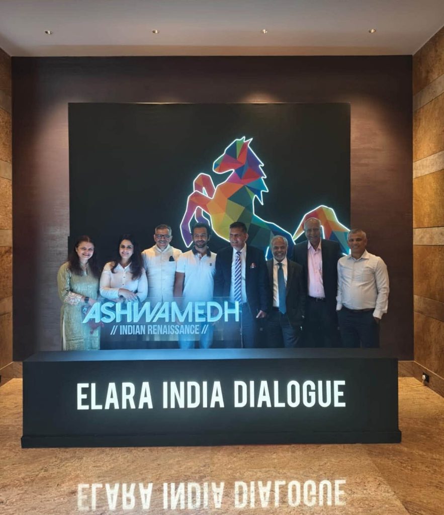 sunder thakur_2 | No. 1 Indian Media News Portal Group of eight professionals posing in front of a colorful geometric horse mural at Elara India Dialogue event signature wall reading ELARA INDIA DIALOGUE.