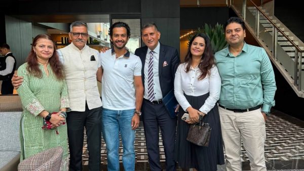 Six people stand together in a modern hotel lobby posing for a group photo in smart casual and business attire.