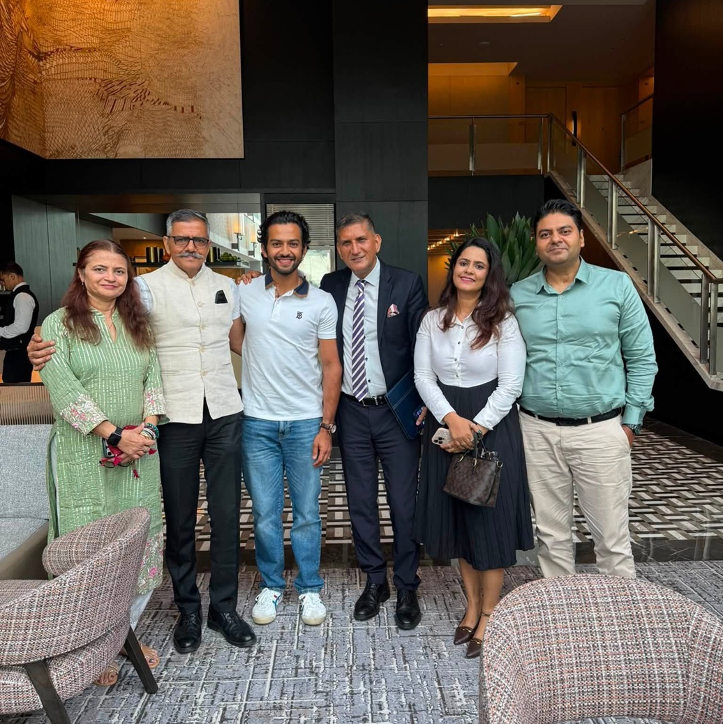 Six people stand together in a modern hotel lobby posing for a group photo in smart casual and business attire.