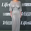 Woman in a shimmering silver gown posing on a green carpet at a high-profile event backdrop with logos (Variety, Lifetime).
