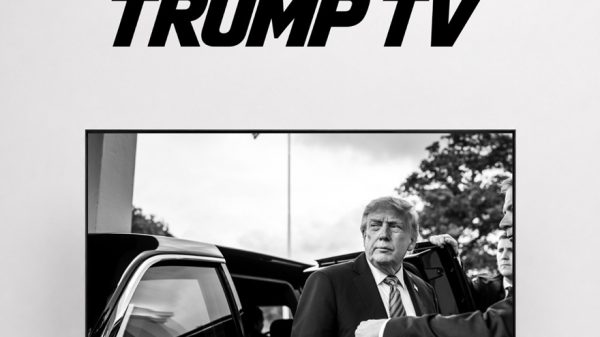 TRUMP TV logo above a black-and-white photo of a man in a suit being escorted toward a car on a TV screen.
