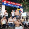 Group of shirtless men sitting on a street at night, with a police officer and a red-blue signboard overhead in Hindi