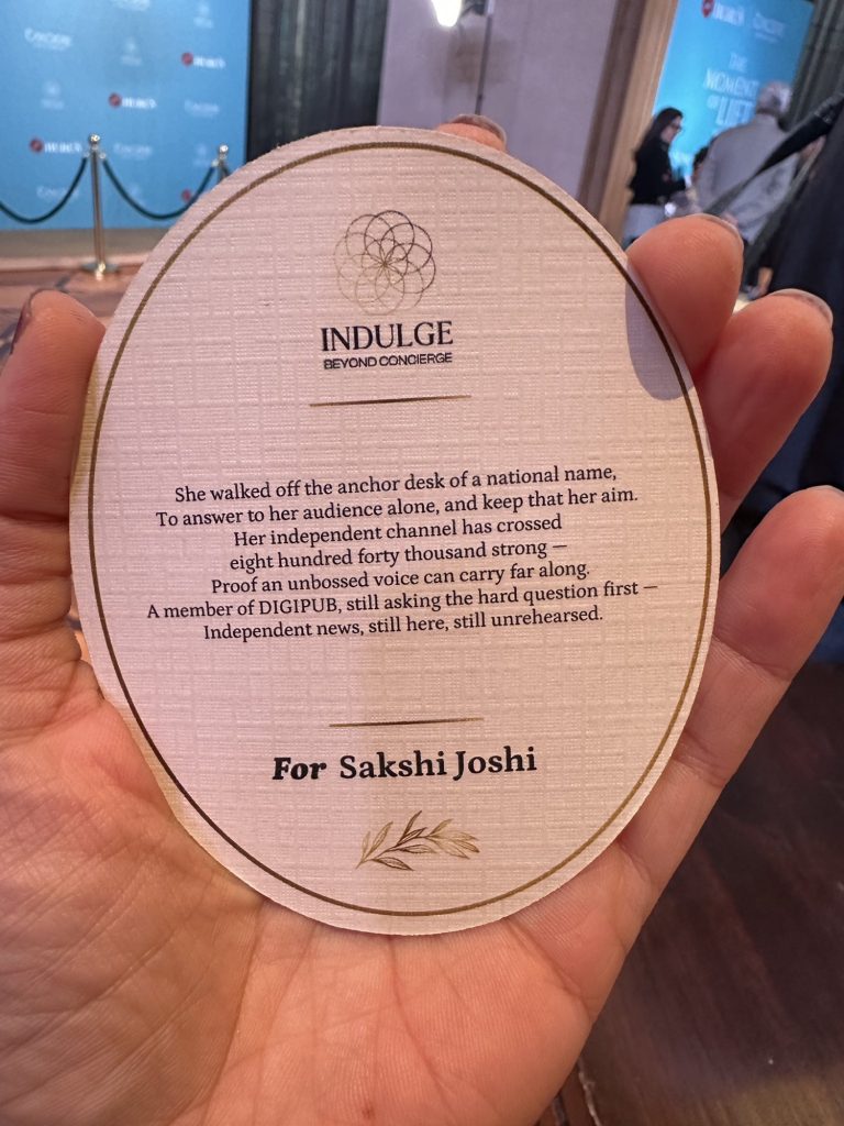 177cb4db-c469-4ed8-a6b4-031ae2fcb004 | No. 1 Indian Media News Portal Round circular badge with 'INDULGE BEYOND CONCIERGE' and dedication 'For Sakshi Joshi' held in a hand at an event/venue.