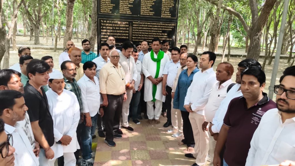24e9de61-8beb-44dc-82e8-f2fb903e0f8e | No. 1 Indian Media News Portal Group of people standing in a park around a dark memorial plaque inscribed with names and text.