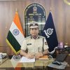Indian security officer in uniform seated at a glass desk, with the Indian flag to his left and a CISF banner behind him, signing documents.
