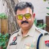 Male police officer in khaki uniform with medals and yellow-tinted sunglasses, standing outdoors.