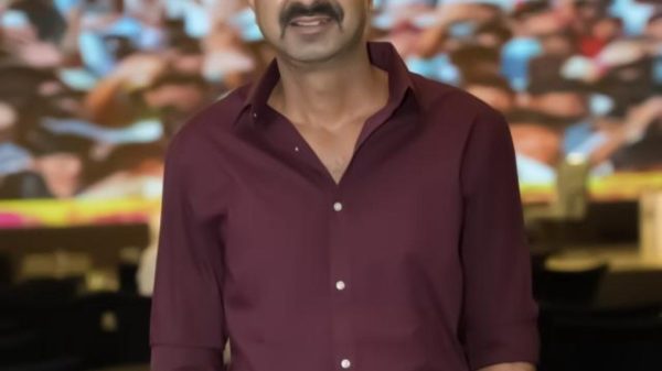 Man in a maroon button-down shirt posing for a photo with a blurred crowd in the background at an event.