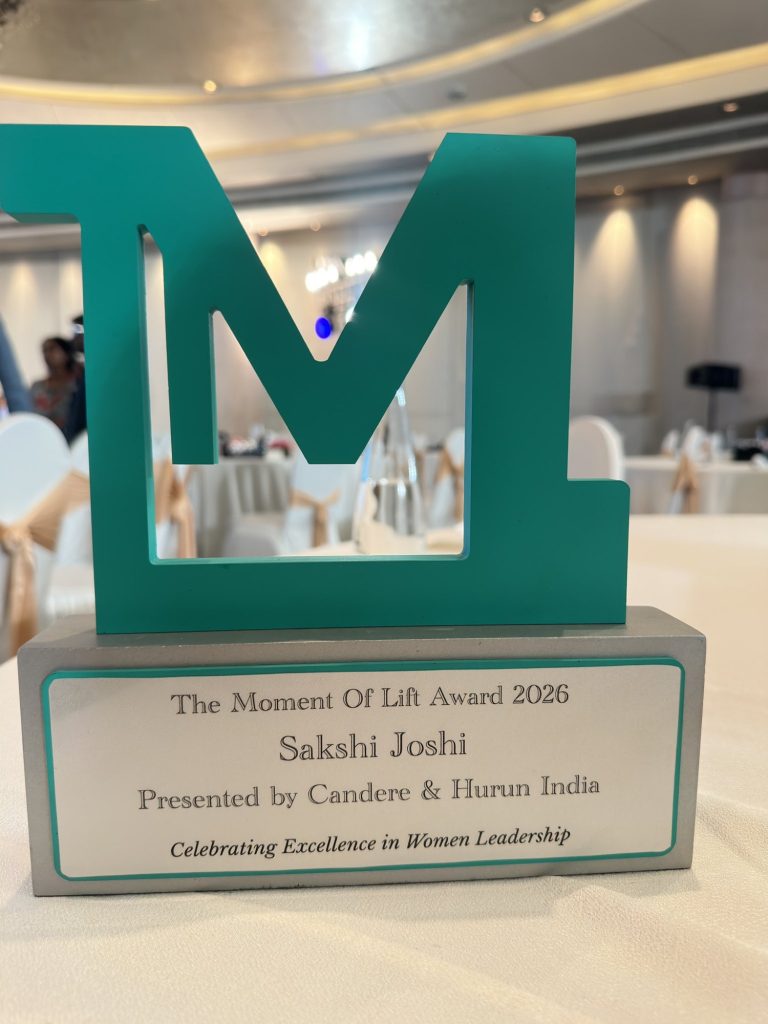 97b44eec-604e-4183-bf8f-8b0f32b2f9fc | No. 1 Indian Media News Portal Turquoise letter 'M' sculpture on a gray base with a plaque reading 'The Moment Of Lift Award 2026' and the recipient's name, Sakshi Joshi.