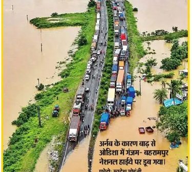 Aerial view of a flooded highway with a long line of stalled trucks and cars as brown floodwater surrounds fields nearby; bold Hindi banner reads 'हाईवे पर पानी, ट्रैफिक थमा' and a news headline about deaths and villages cut off.