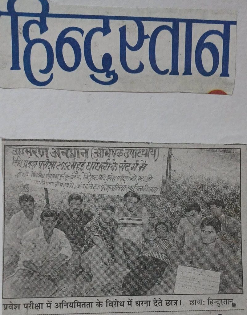Black-and-white photo of students sitting on the ground with a banner behind them, protesting about inequality in entrance exams.