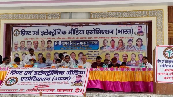 Panel of officials seated at a long table on a stage, with a large Hindi banner and portraits behind them, during a conference.